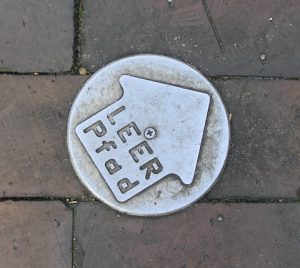 Metallene Markierungen auf dem Straßenpflaster weisen den Weg zur nächsten LEER-Pfad-Station, an der jeweils ein stadtökologisches Thema behandelt wird